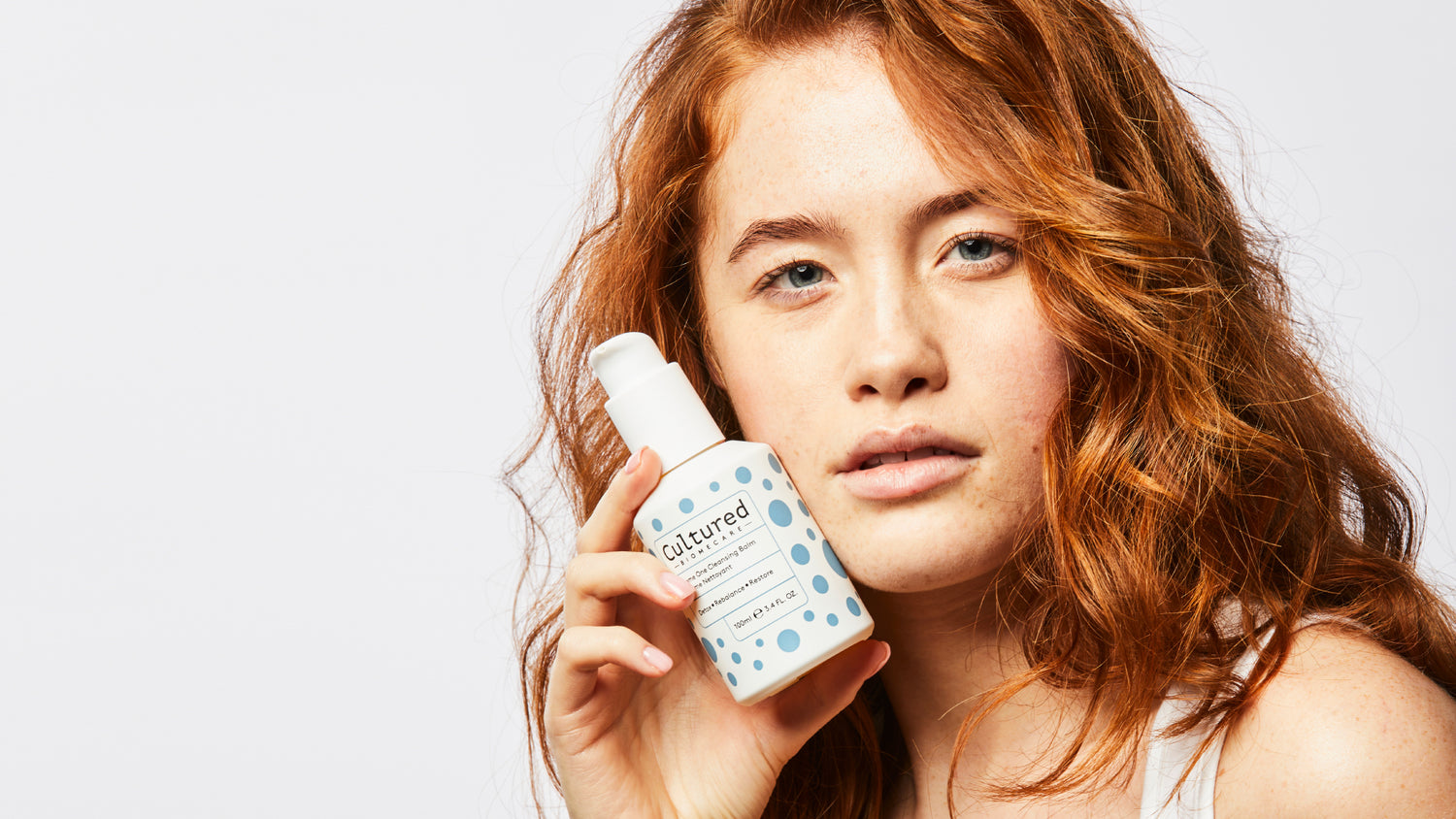 A close-up photo of a model holding the Biome One Cleansing Balm close to her face.