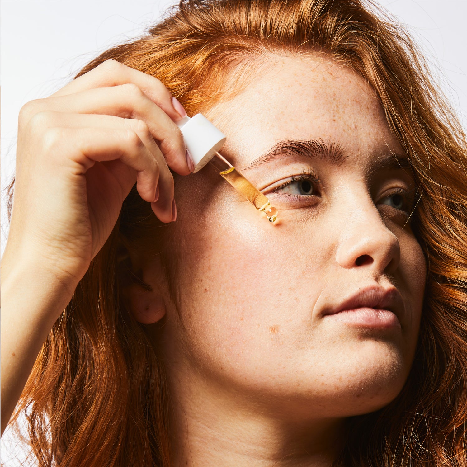 Eye level headshot of a model looking to the side & holding a pipette of Cultured Biomecare product to their cheekbone.