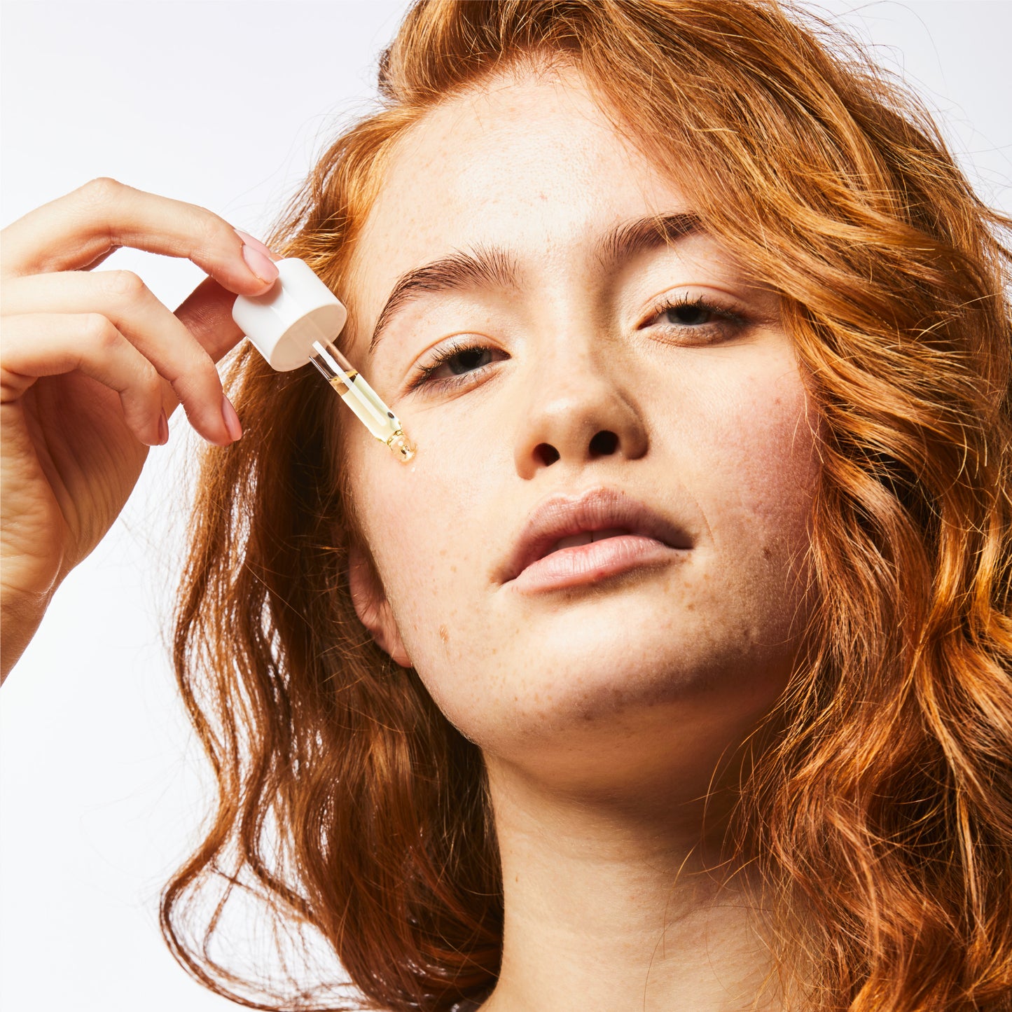 Close up of woman holding oil serum pipette on her cheek