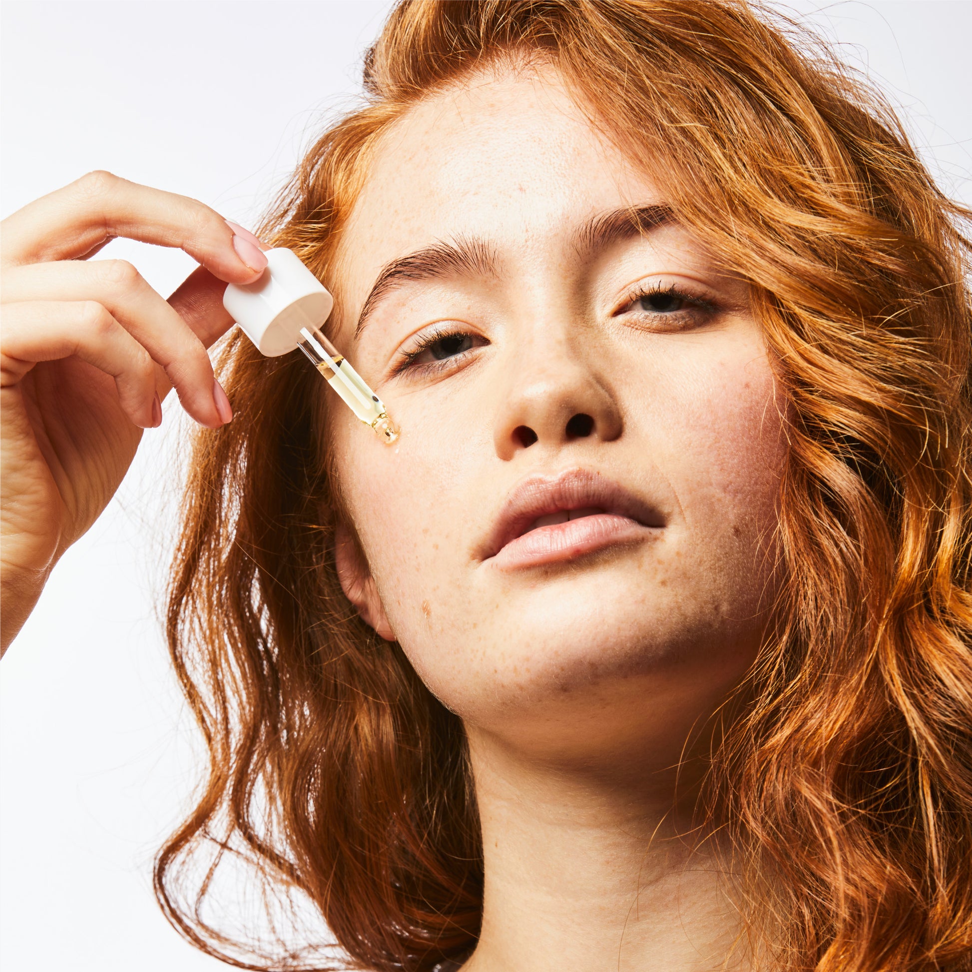 Close up of woman holding oil serum pipette on her cheek