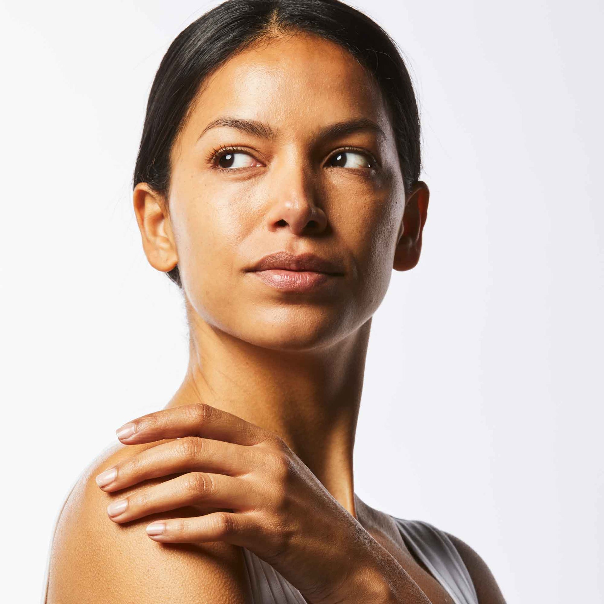 Woman posing with glowing skin, touching her shoulder