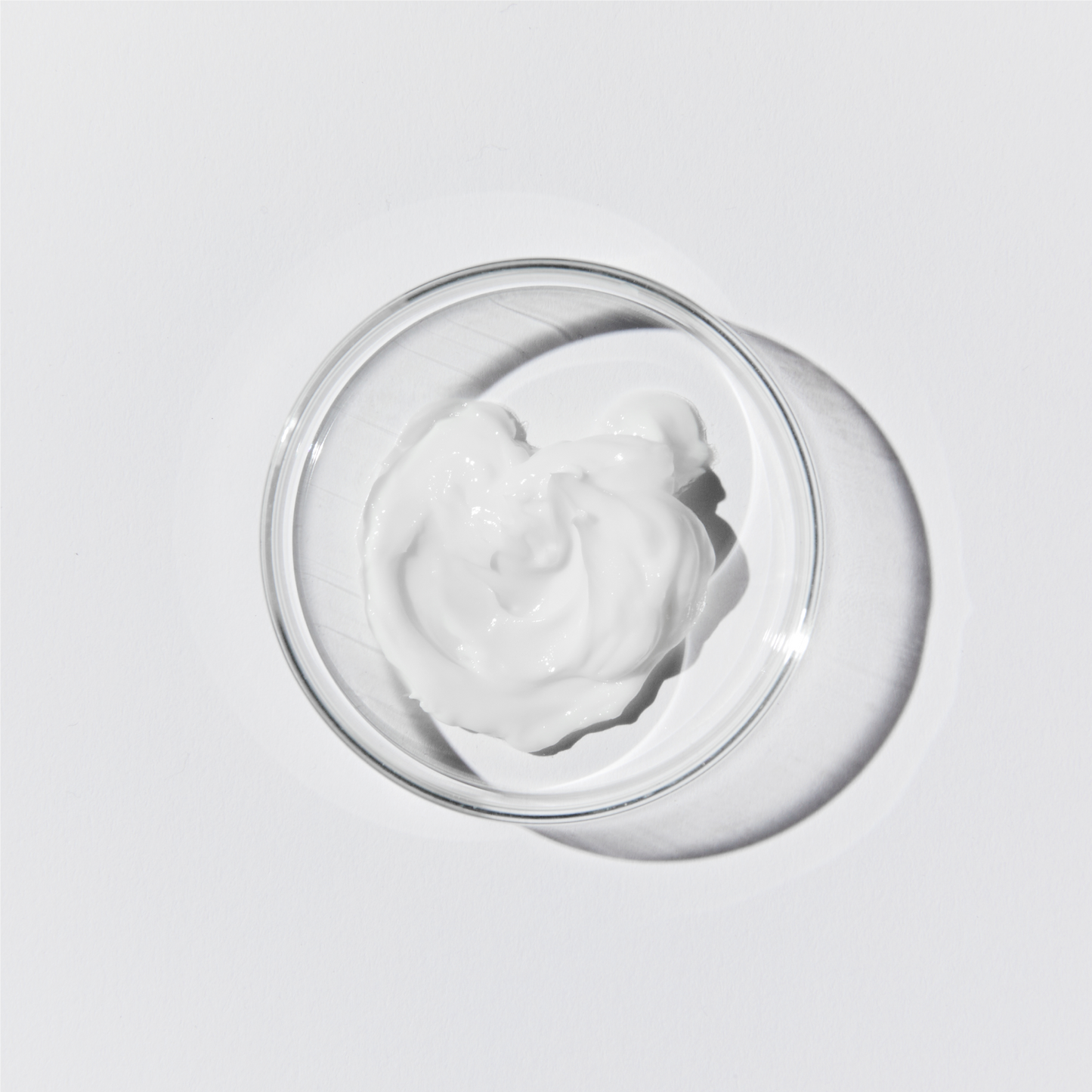 Aerial shot of the calm cream. Its an opaque, white liquid in a petri dish against a white background.