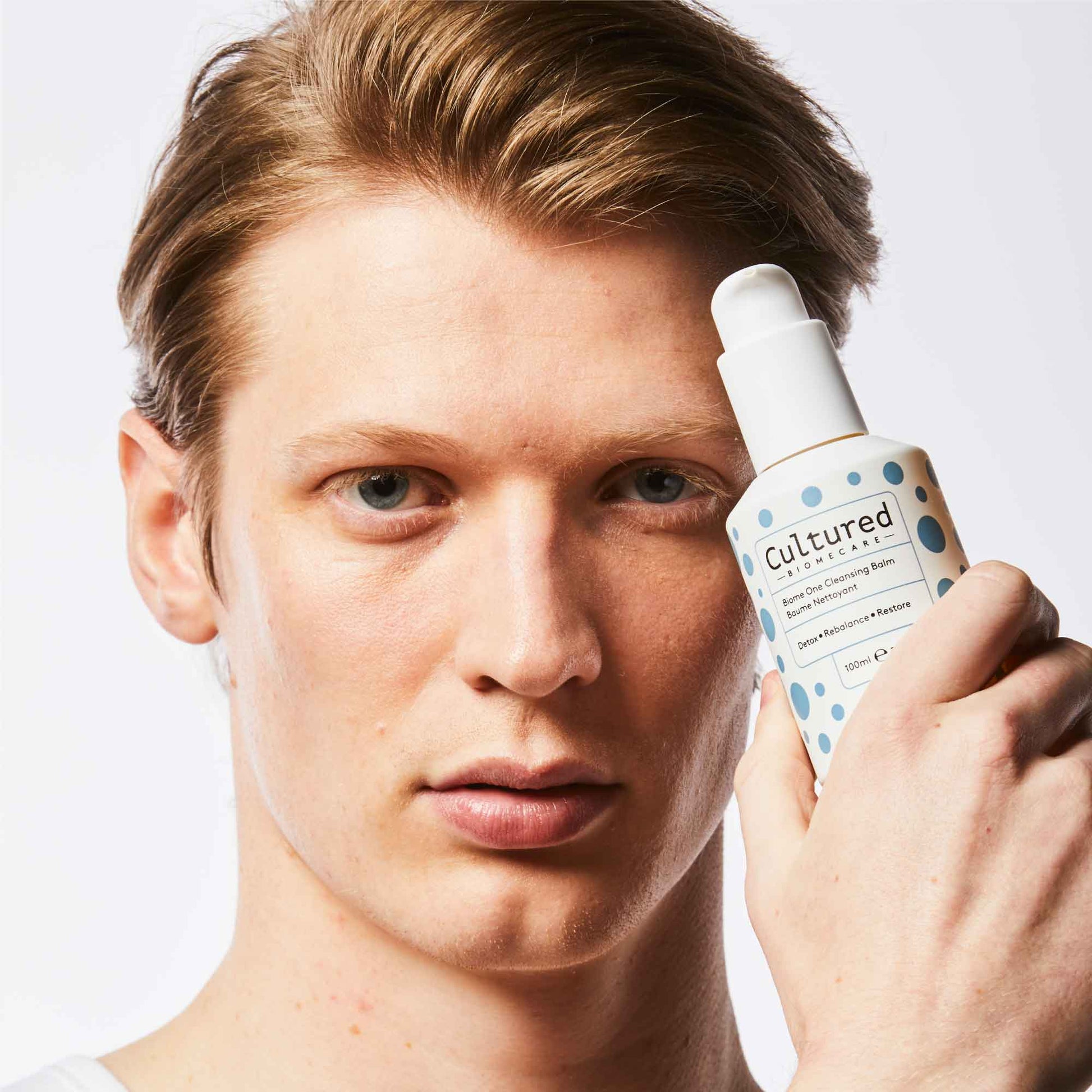 a young man holds a bottle of the Cleansing Balm looking at the camera