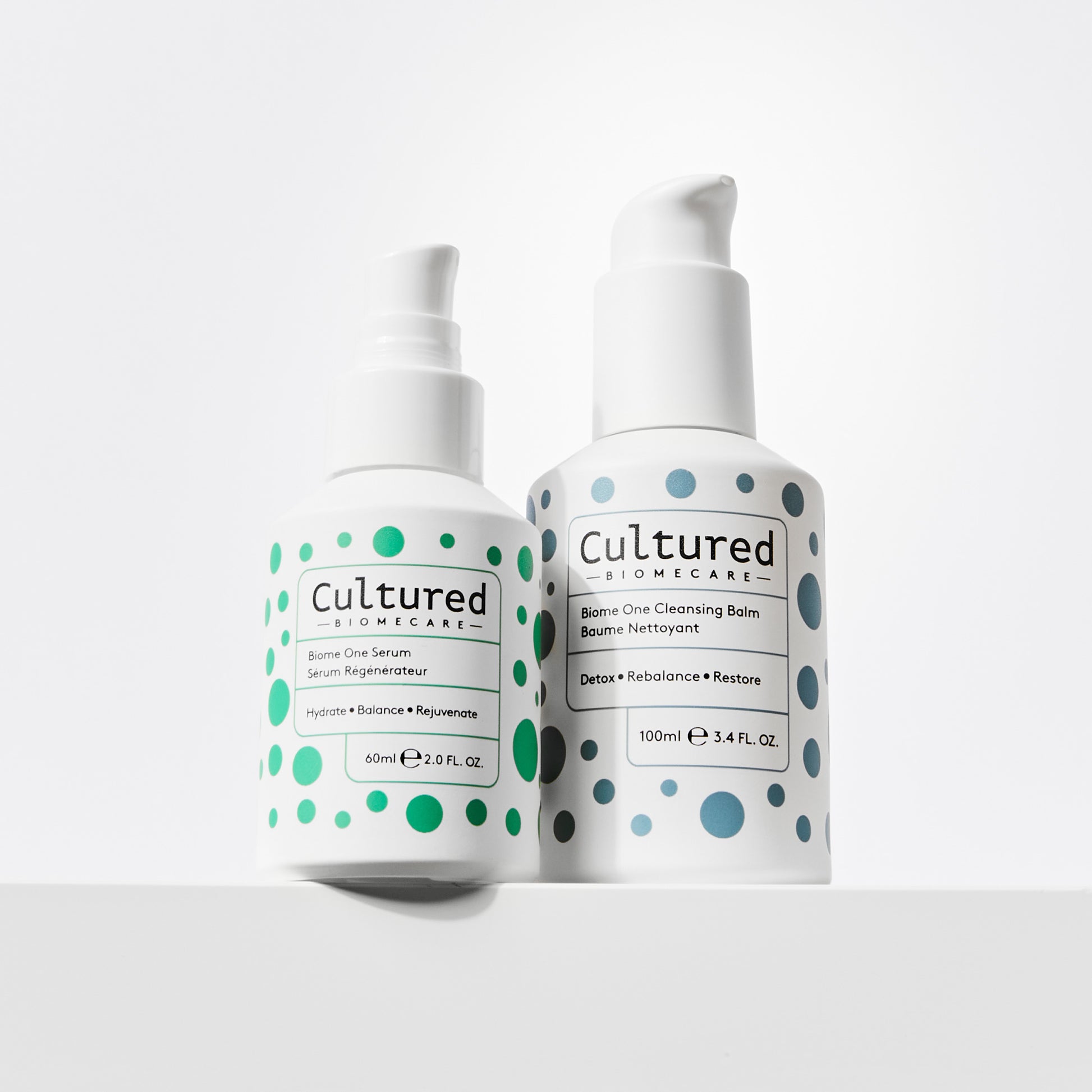 Cultured Biomecare Biome One Serum and Cleansing Balm sit side by side on a white shelf against a white background.