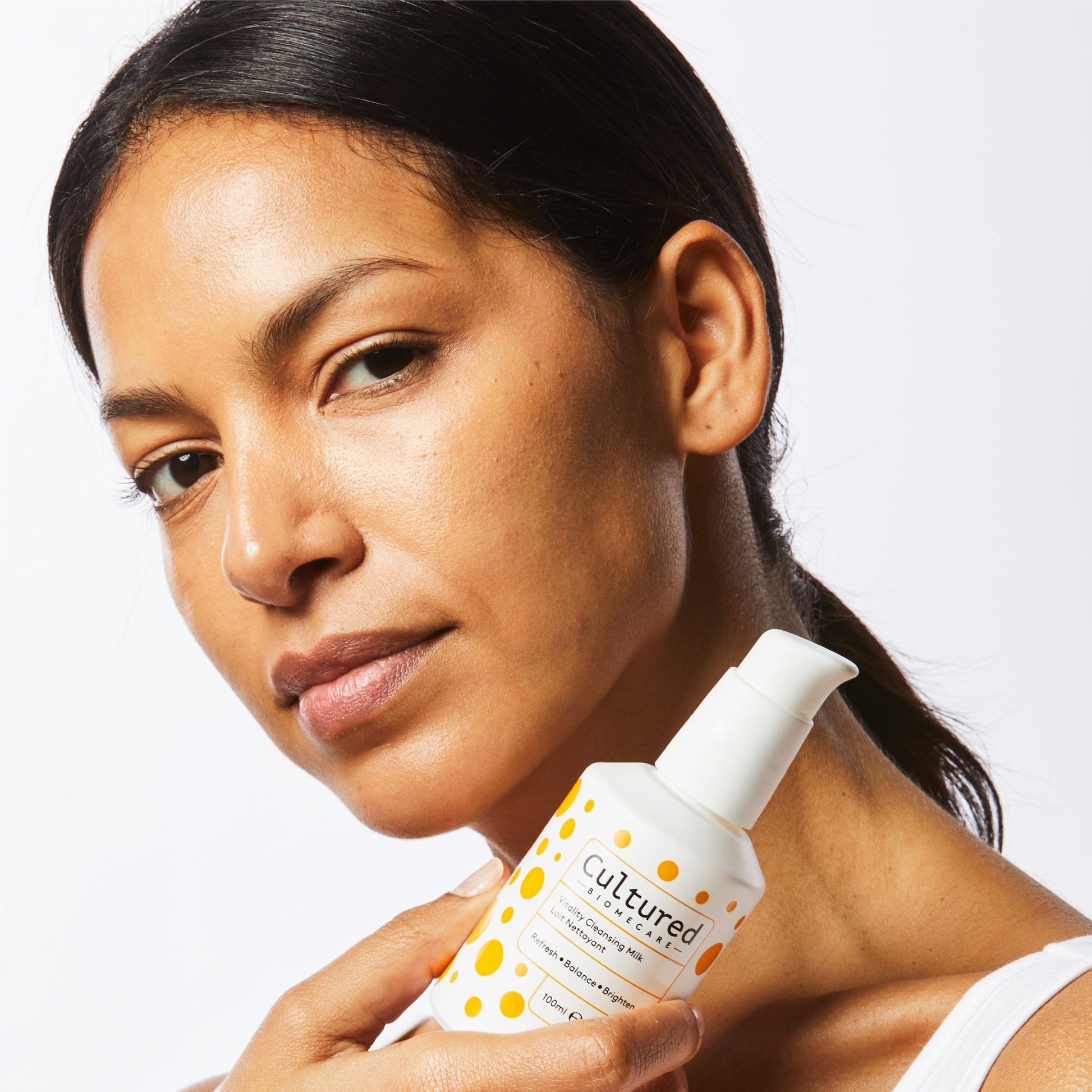A close up headshot of a model with clear, glowing skin holding the Cleansing Milk up to her face.