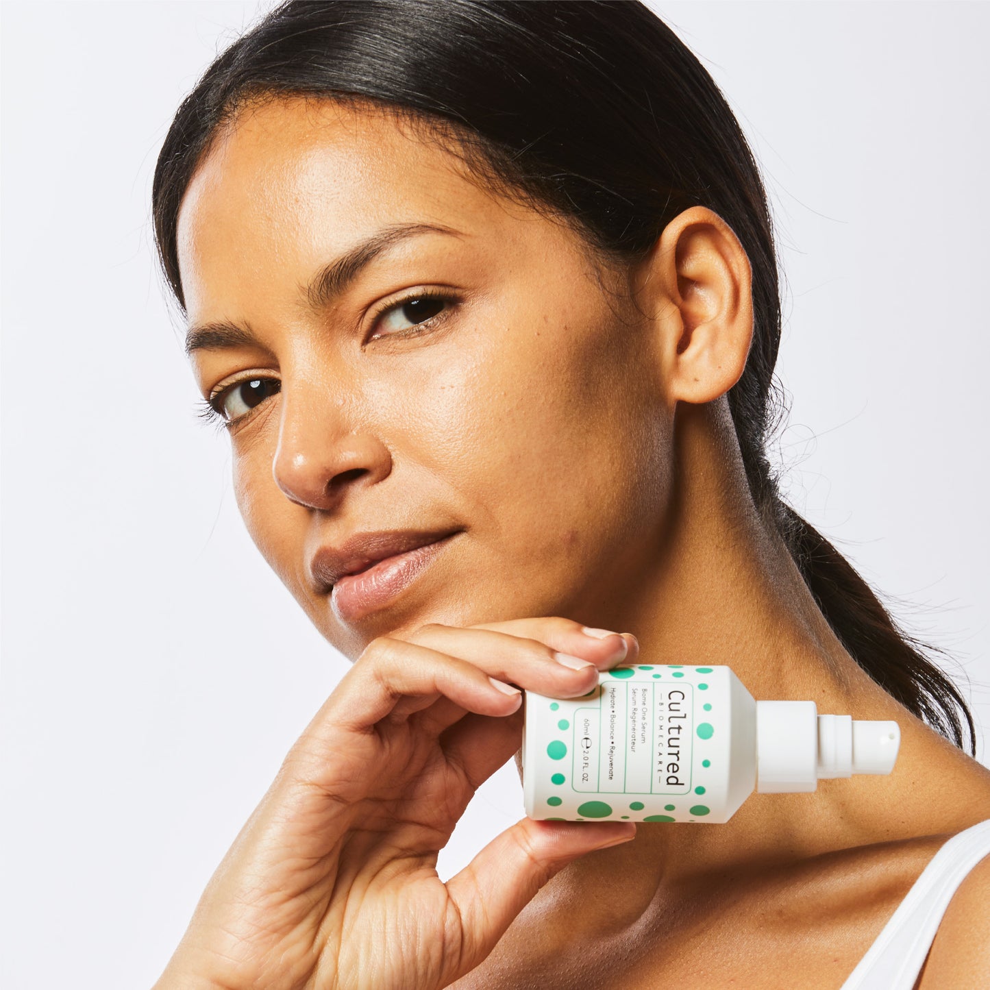 A close up headshot of a model with clear, glowing skin holding the Biome One Serum up to her face.