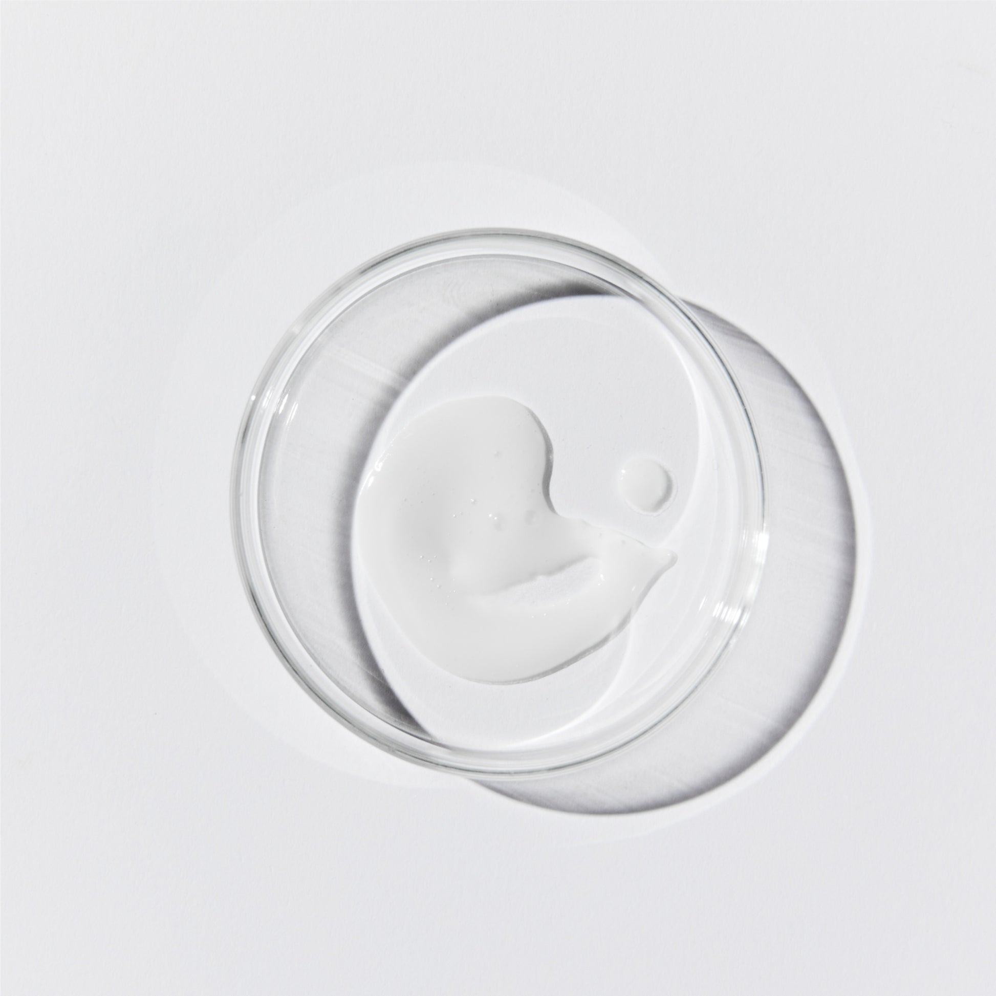 Aerial shot of the serum. Its an opaque, white liquid in a petri dish set against a white background.